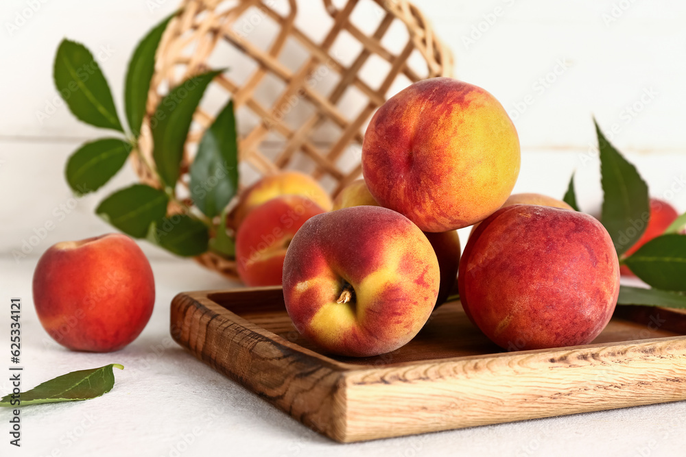 Wooden board with sweet peaches and leaves on white table