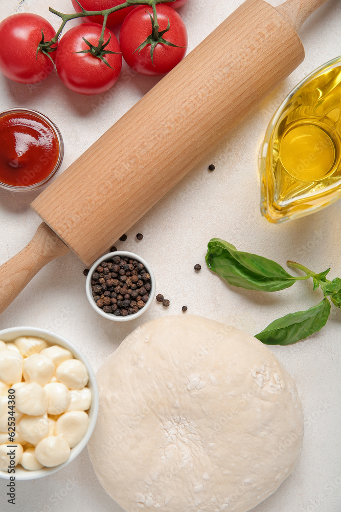 Raw dough and ingredients for preparing pizza on light background