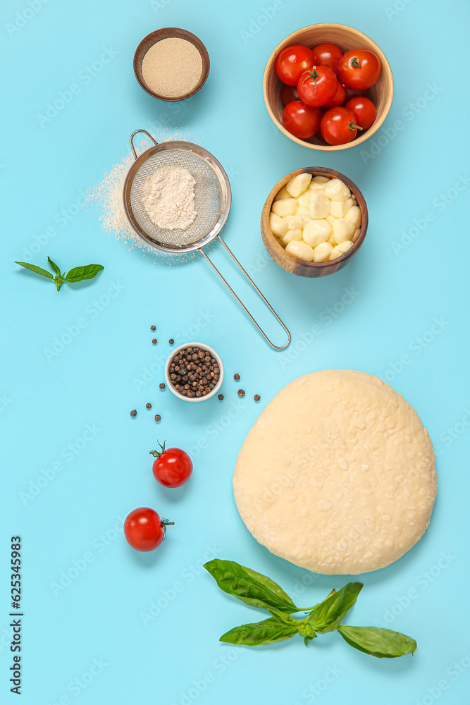 Raw dough and ingredients for preparing pizza on blue background