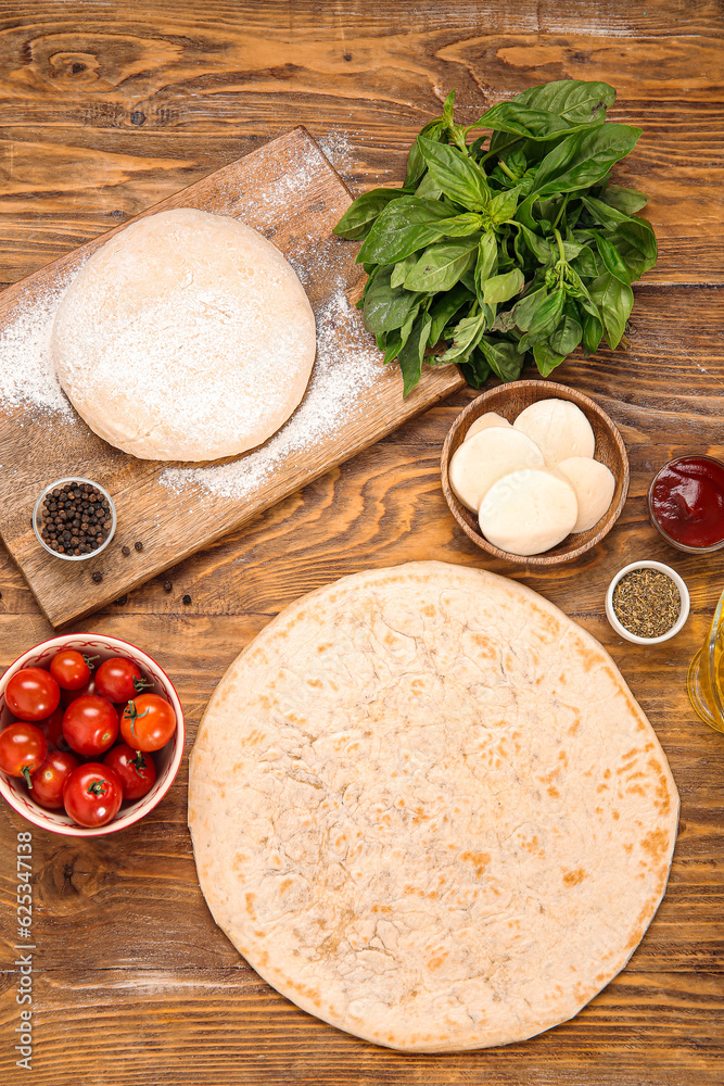 Raw dough, crust and ingredients for preparing pizza on wooden background