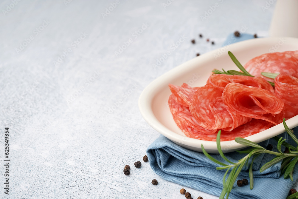 Bowl with slices of tasty salami on light background