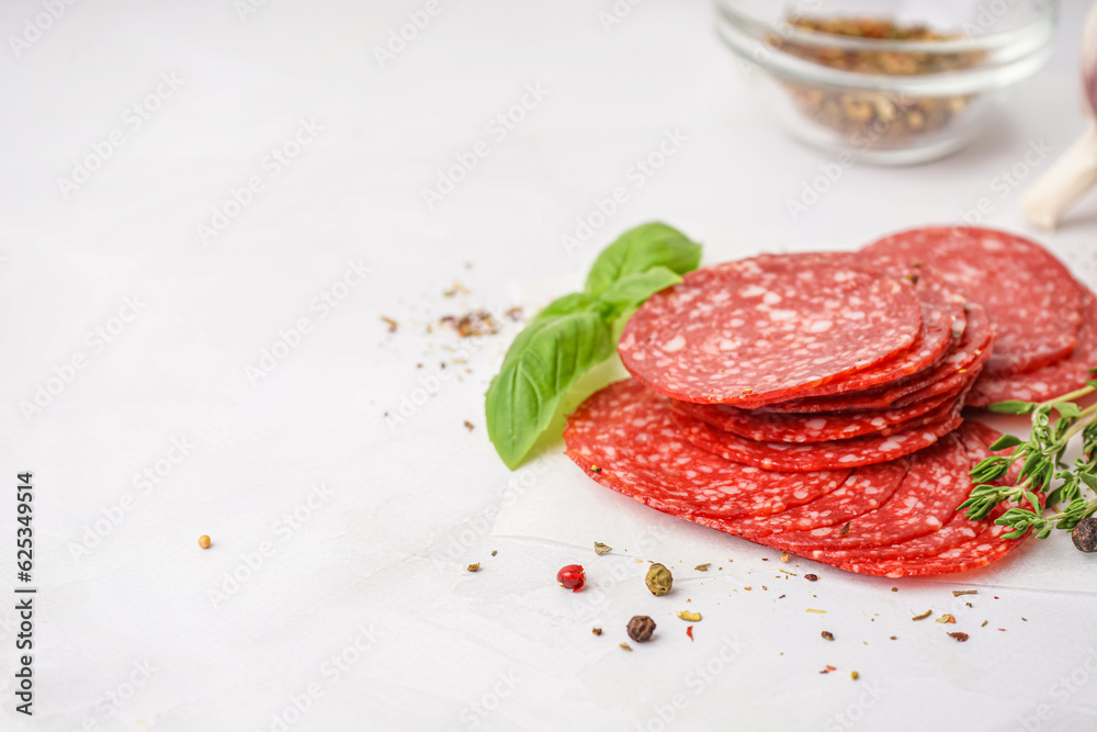 Slices of tasty salami on light background