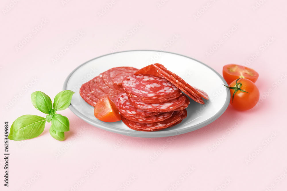 Plate with slices of tasty salami on pink background