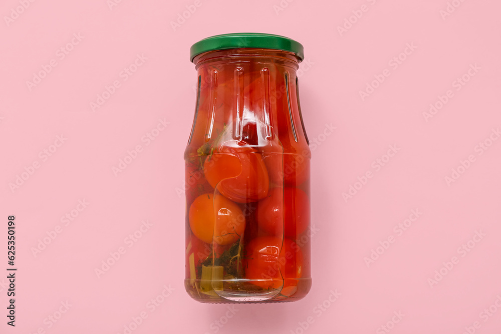 Jar with canned tomatoes on pink background