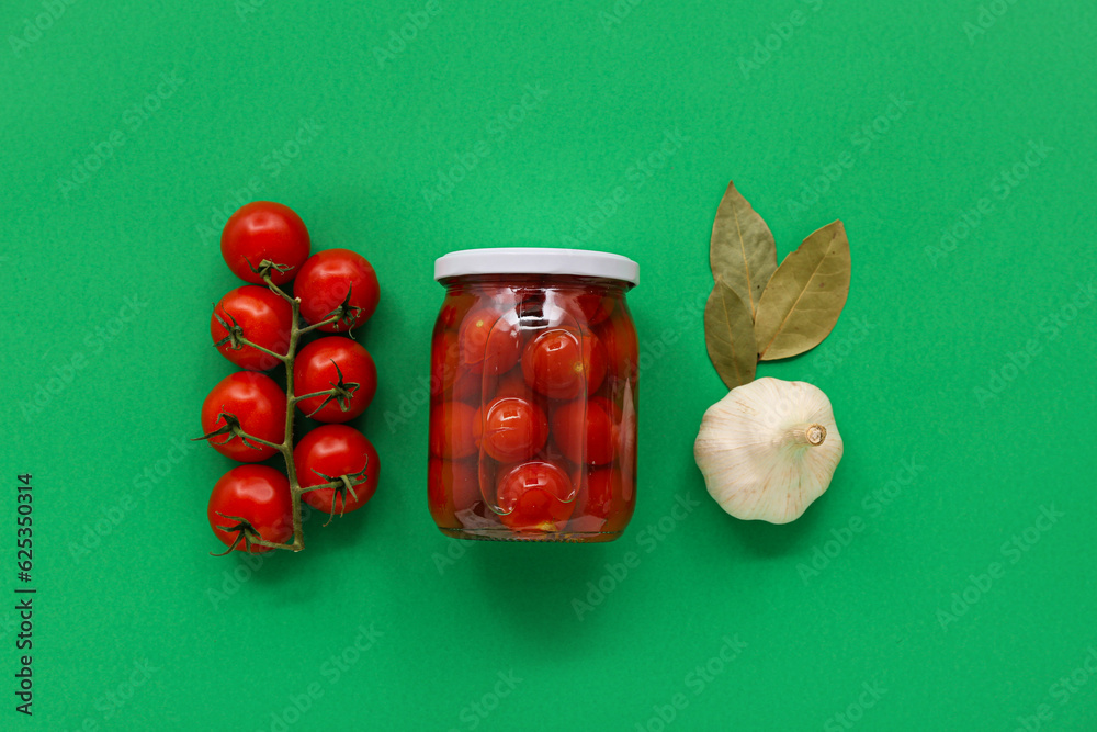 Jar with canned tomatoes and garlic on green background