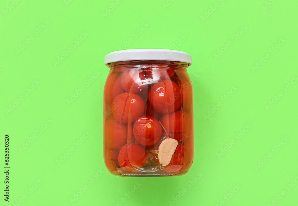 Jar with canned tomatoes on green background