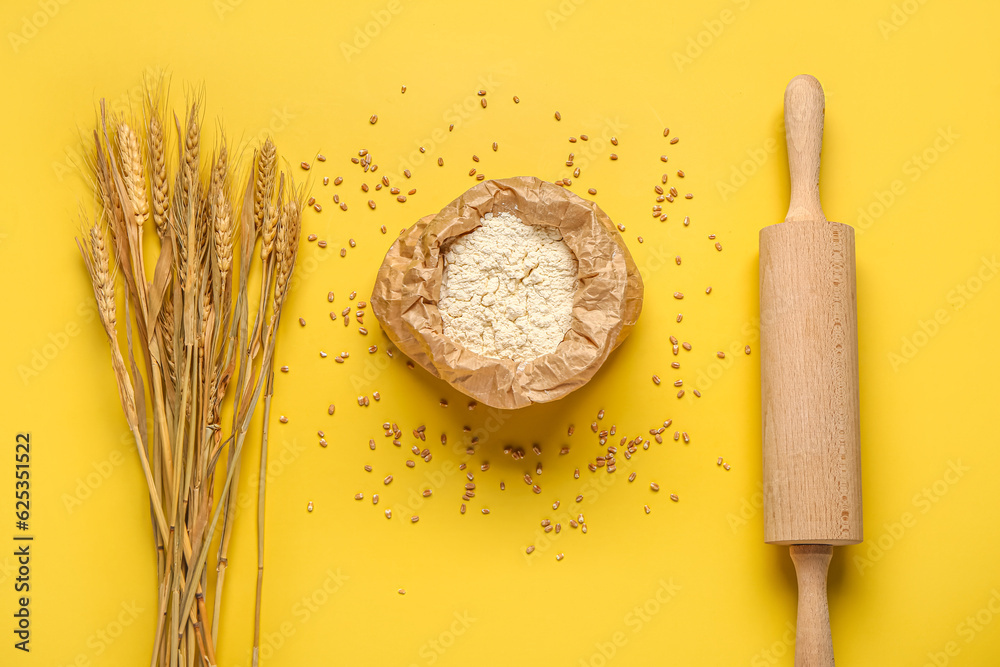 Bag of flour, rolling pin and wheat ears on yellow background