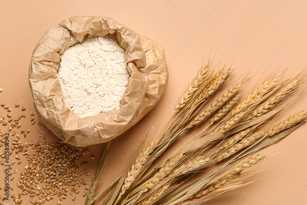 Bag of flour, wheat ears and grains on beige background