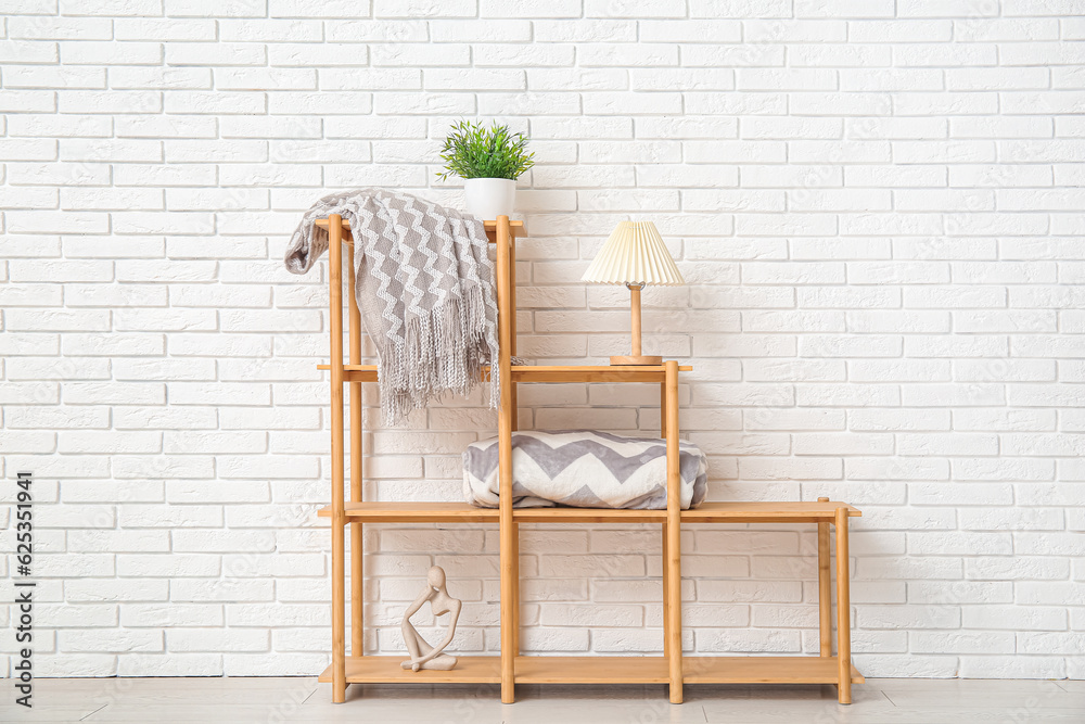 Shelving unit with cozy blankets near white brick wall