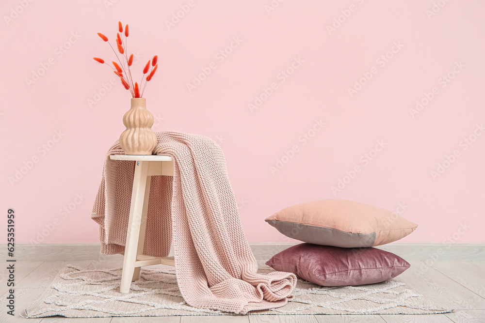 Vase with dried flowers and blanket near pink wall