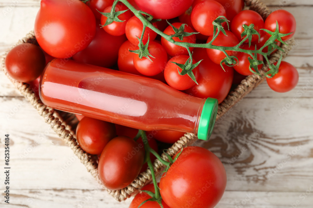 Wicker box with fresh tomatoes and bottle of juice on light wooden background