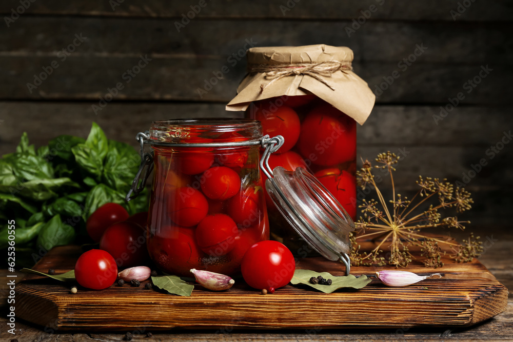 Jars with canned tomatoes and basil on wooden background