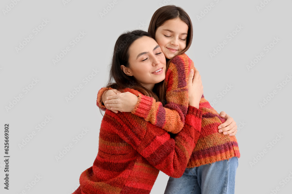 Little girl and her mother in warm sweaters hugging on grey background