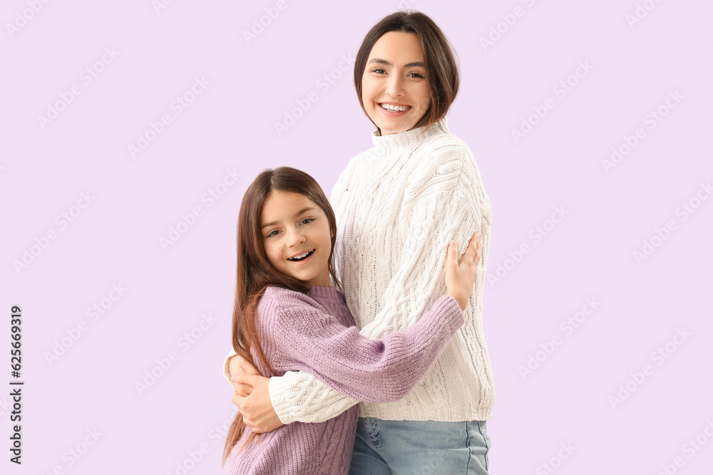 Little girl and her mother in warm sweaters hugging on lilac background