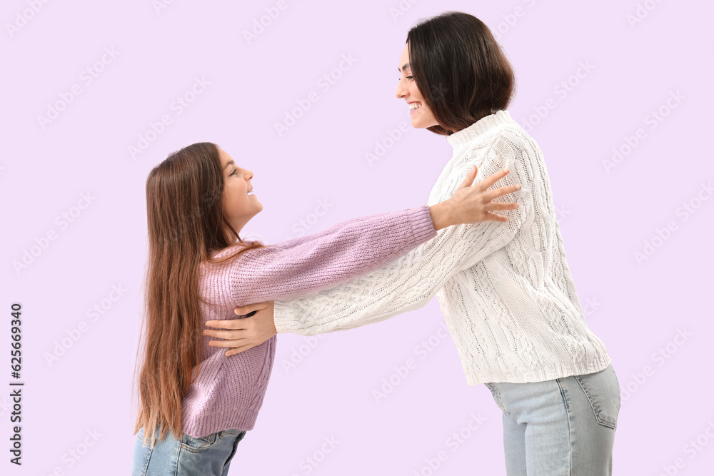 Little girl and her mother in warm sweaters hugging on lilac background