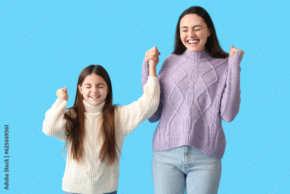 Happy little girl and her mother in warm sweaters on blue background