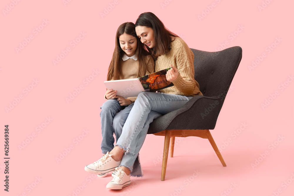 Little girl and her mother reading book in armchair on pink background