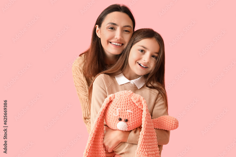 Little girl and her mother in warm sweaters with toy bunny on pink background