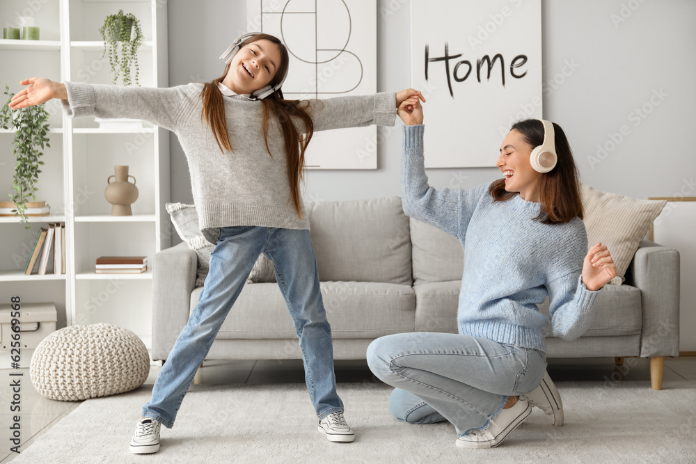 Little girl and her mother in sweaters and headphones dancing at home