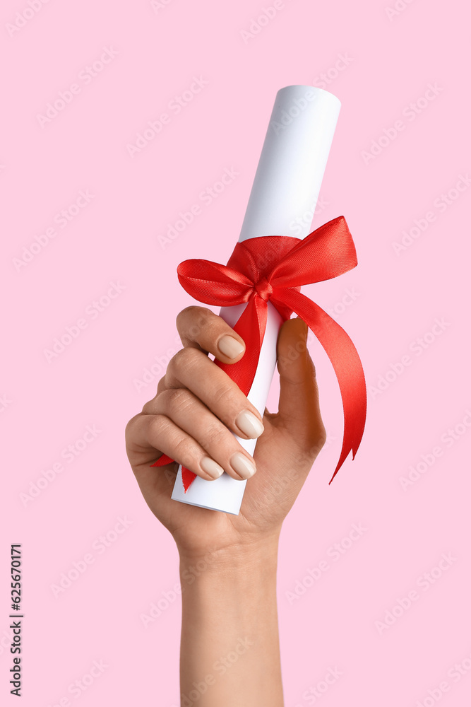 Woman holding diploma with ribbon on pink background