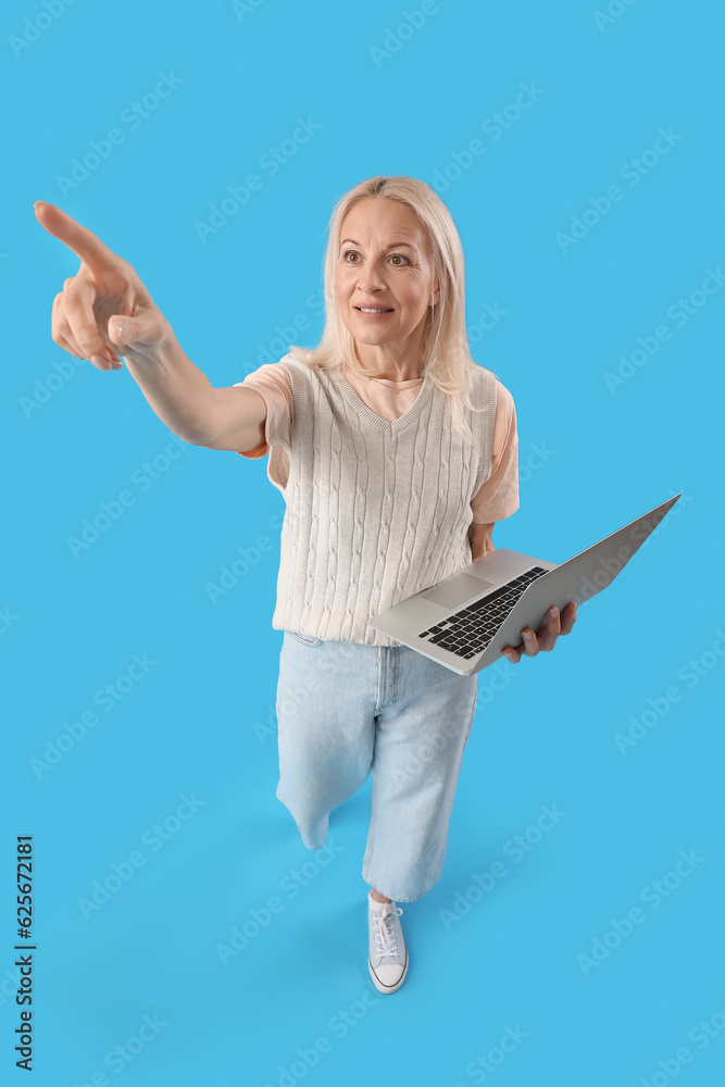 Mature female programmer with laptop pointing at something on blue background