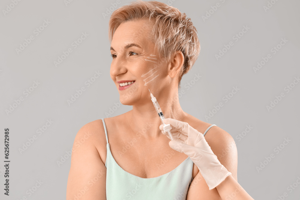 Mature woman receiving filler injection on light background, closeup