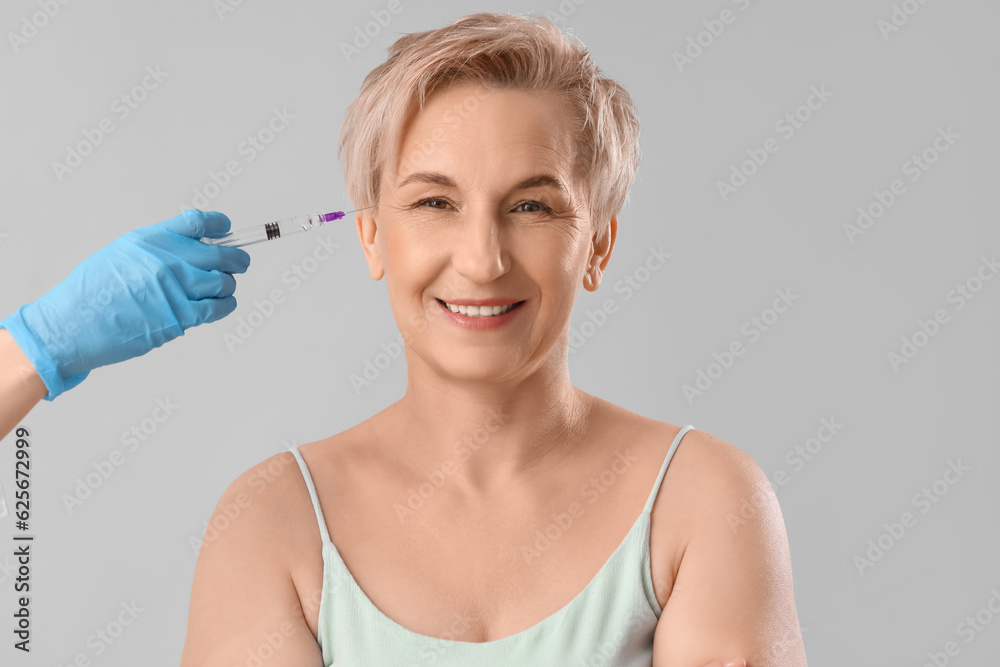 Mature woman receiving filler injection on light background