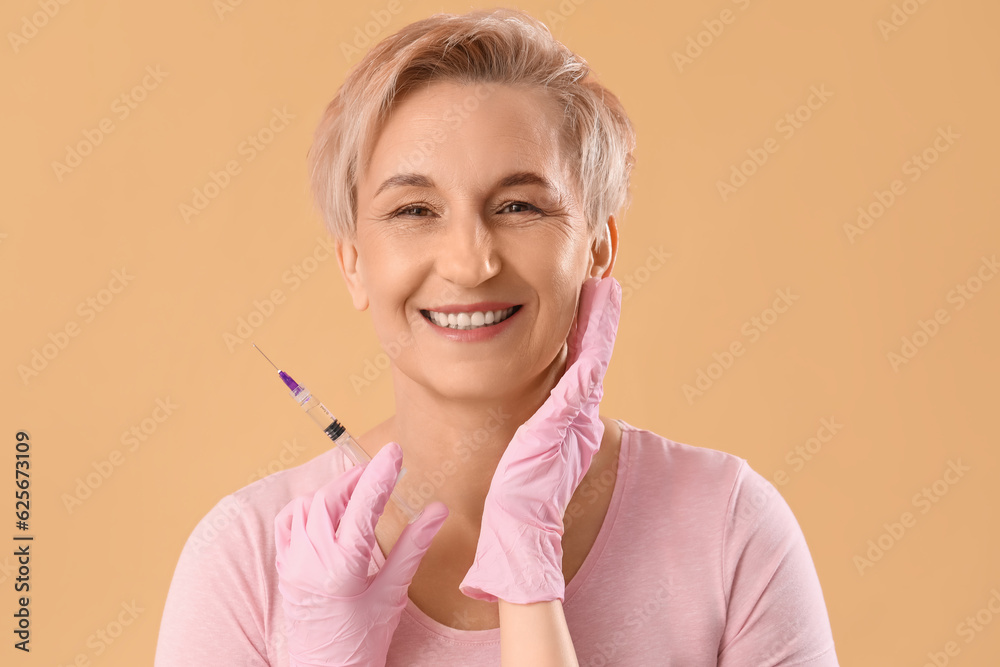 Mature woman and beauticians hands with filler injection on beige background, closeup