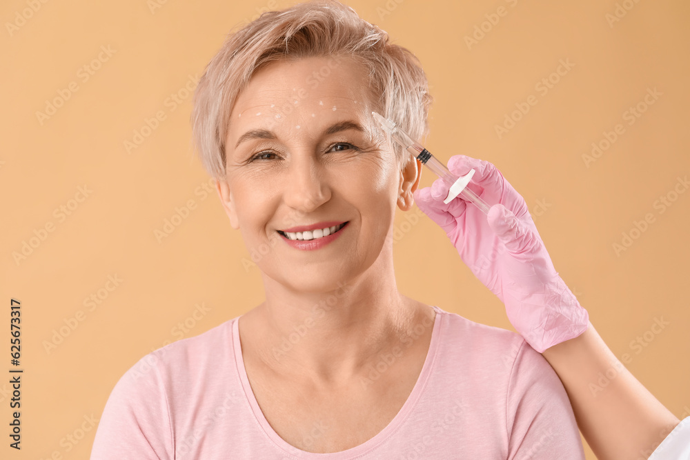 Mature woman receiving filler injection on beige background, closeup