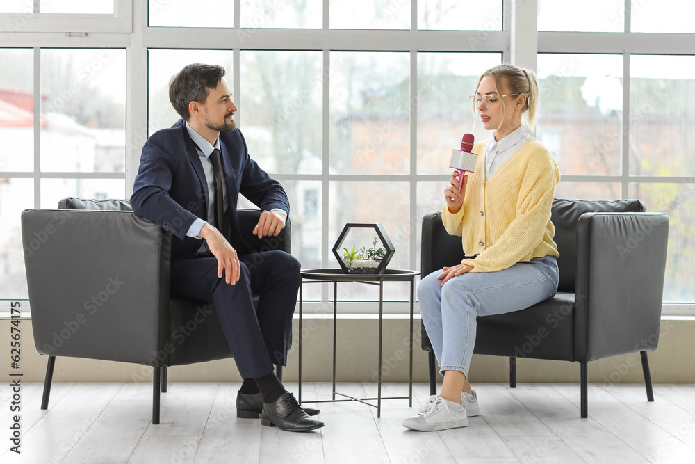 Female journalist with microphone having an interview with man in office