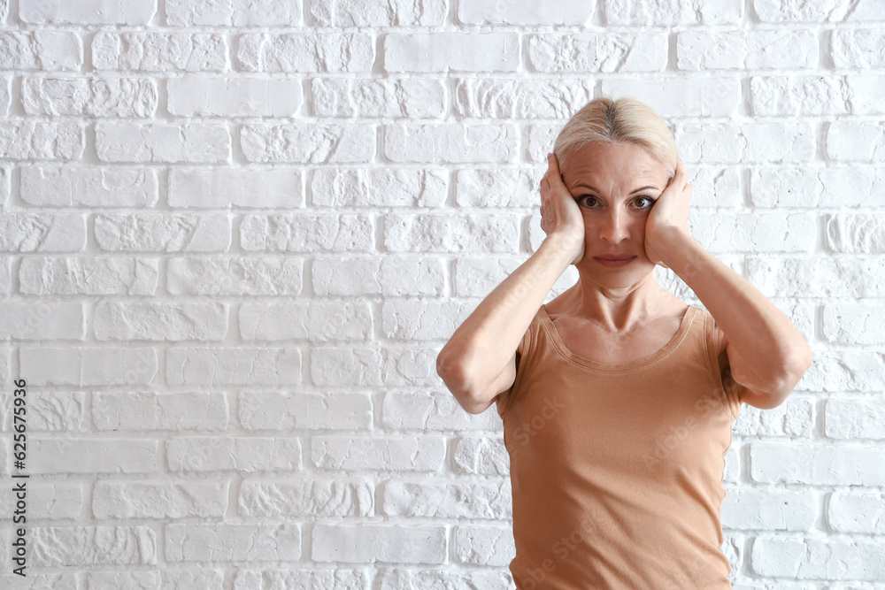 Mature woman doing face building exercise on white brick background