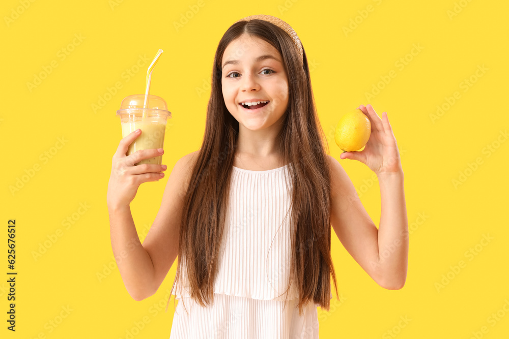 Little girl with glass of smoothie and lemon on yellow background