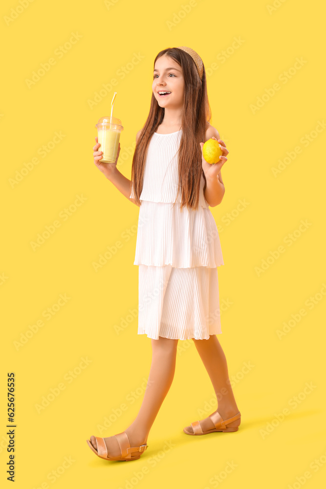 Little girl with glass of smoothie and lemon on yellow background