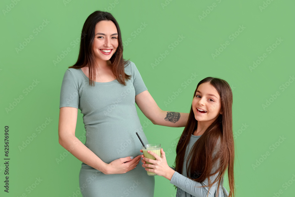 Little girl with glass of smoothie and her pregnant mother on green background