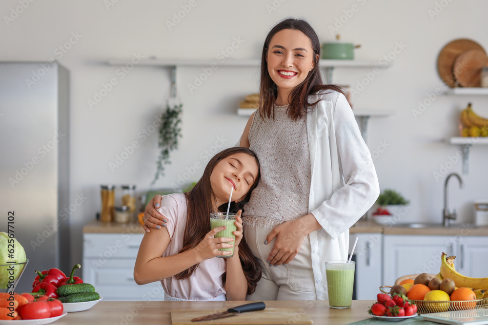 Little girl with her pregnant mother drinking green smoothie in kitchen