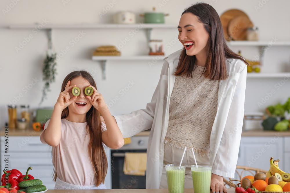 Little girl with her pregnant mother drinking green smoothie in kitchen