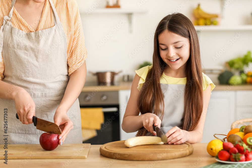 Little girl with her mother cutting fruits for smoothie in kitchen