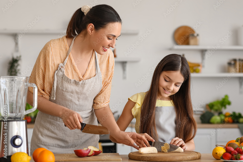 Little girl with her mother cutting banana for smoothie in kitchen