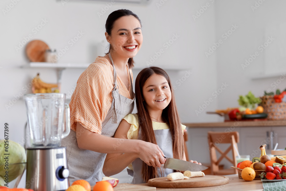 Little girl with her mother cutting banana for smoothie in kitchen