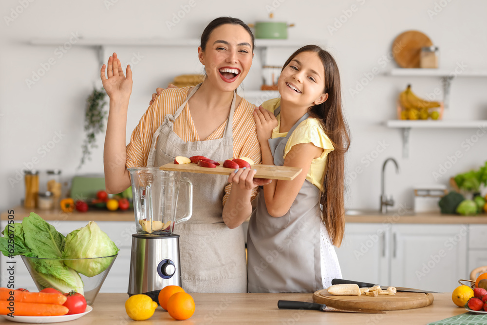 Little girl with her mother putting cut apple into blender in kitchen