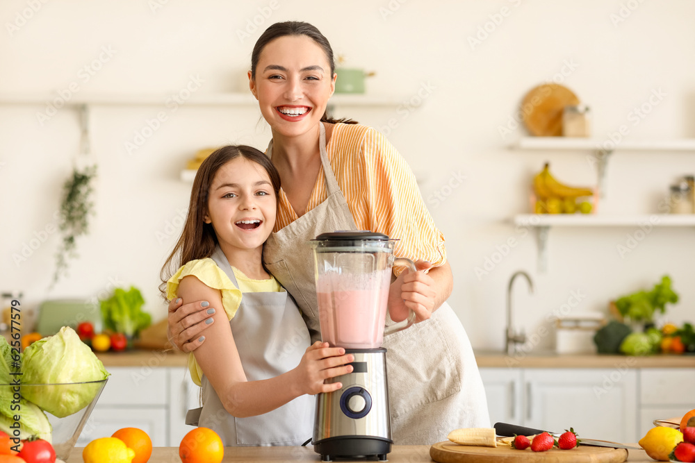 Little girl and her mother making smoothie with blender in kitchen