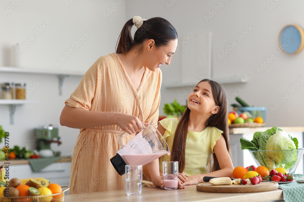 Young woman with her little daughter pouring fresh smoothie into glass in kitchen