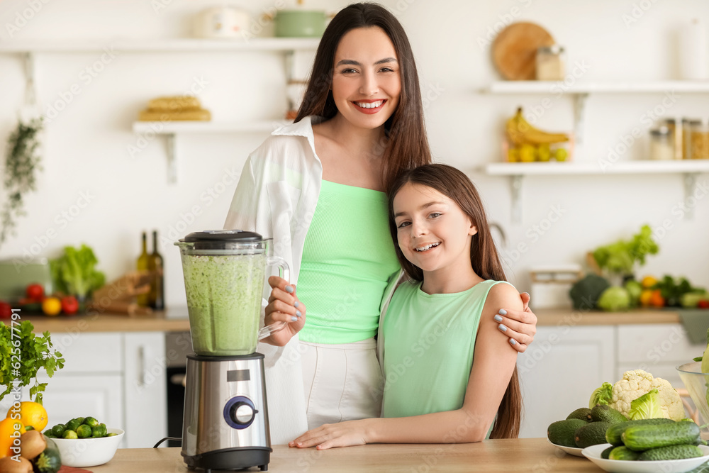 Little girl and her mother making vegetable smoothie with blender in kitchen