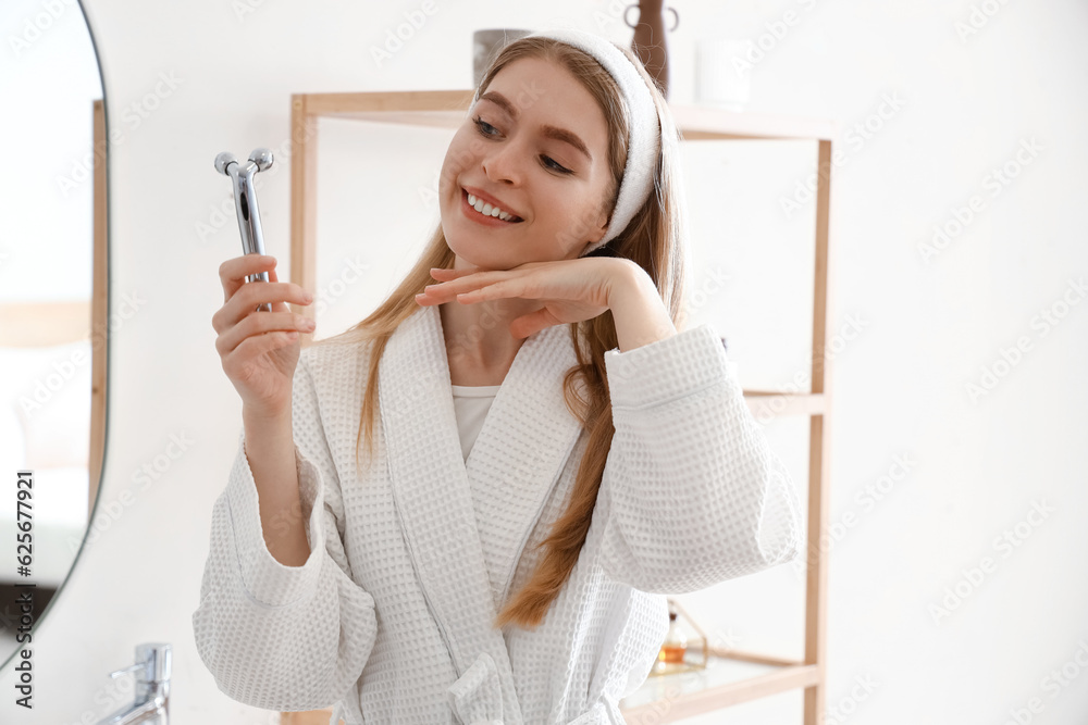 Young woman with facial massage tool in bathroom