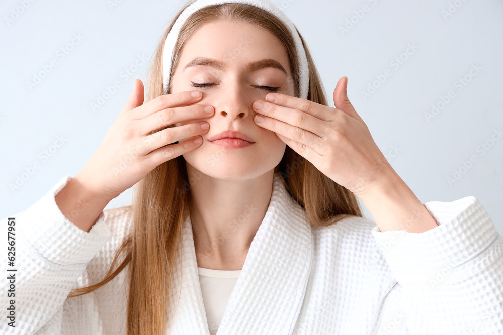 Young woman doing face building exercise on light background, closeup