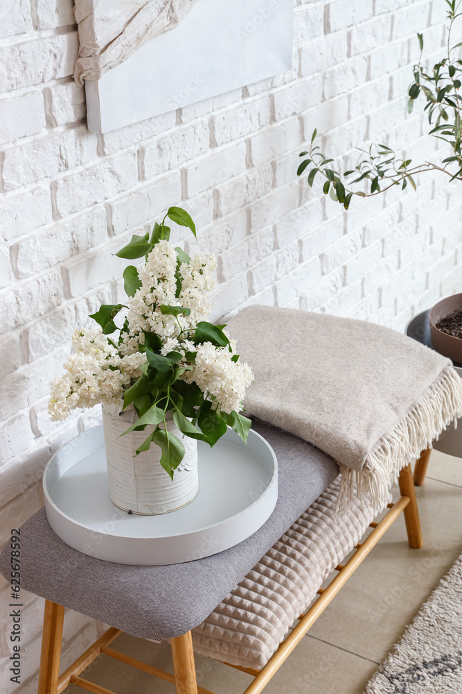 Vase with lilac flowers on soft bench in room