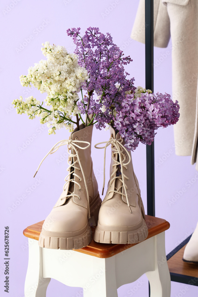 Stylish boots with lilac flowers on stool in hall