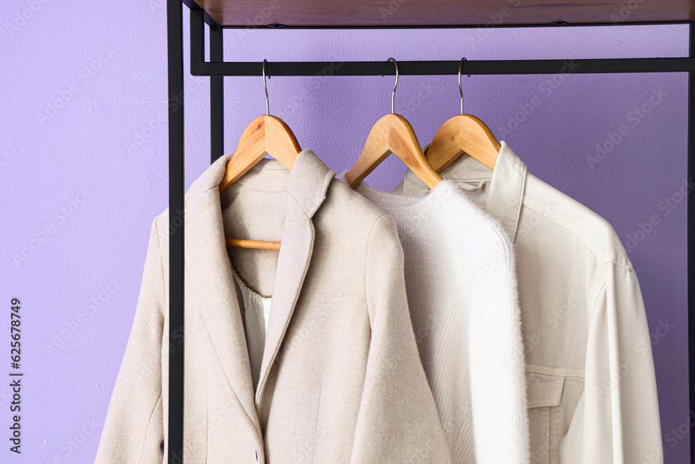 Stylish clothes hanging near lilac wall in hall, closeup