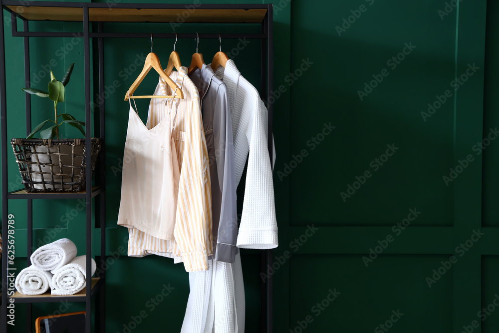 Shelving unit with clothes, towels and houseplant near green wall