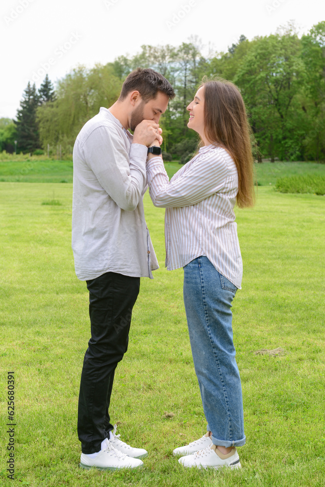 Young man kissing his girlfriends hands in beautiful park